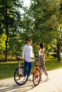 Vertical photo of cheerful couple of bicyclists are having conversation in the park and they are glad to meet each other.