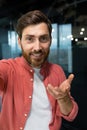 Vertical photo. Close-up photo. Young man freelancer, blogger in red shirt greets and talks to the camera, smiles, waves Royalty Free Stock Photo