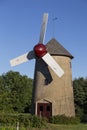 Concrete windmill with cedar shingled roof, red and white sails and dark red door Royalty Free Stock Photo