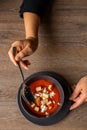 Vertical photo of cropped woman hands stir red tomato cream soup with soup crouton toasts on black plate on wooden table Royalty Free Stock Photo