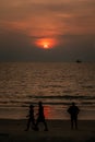 Vertical photo of Dramatic red sunset, Sun behind foggy clouds, silhouettes of walking man and women, one man standing at seashore
