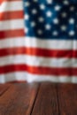 Vertical photo of an empty wooden table in front of the blurred American flag. Independence day concept Royalty Free Stock Photo