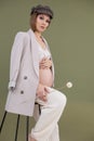 Vertical photo of fashionable pregnant woman in cap, lace cloth, sitting bar chair. Holding stick herbarium. Health care