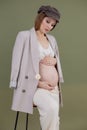 Vertical photo of fashionable pregnant woman in cap, sitting on bar chair. Holding decor stick. Hypertension problem