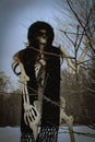 Vertical photo of a female skeleton wearing sunglasses, hat and scarf that is standing outside with the snow falling on her