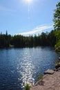 Vertical photo of a forest lake with calm clear water on a summer day. A sunny path sparkles on calm water Royalty Free Stock Photo