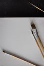 Vertical photo four small paint brushes scattered on white canvas