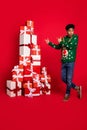 Vertical photo of guy direct finger large pile christmas presents wear green deer pullover isolated on red background