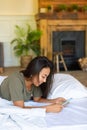 Vertical photo of a happy laughing Asian woman lies in bed with mobile phone. She received a declaration of love from Royalty Free Stock Photo