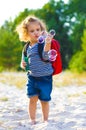 Vertical photo of a little curly girl with a red backpack and soap bubbles on the beach Royalty Free Stock Photo