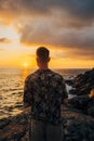 Vertical photo of a man sitting on a cliff at the sunset near the ocean Royalty Free Stock Photo