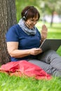 Vertical photo of a middle-aged woman enjoying online talking with her friends and kids. She saying hello with a palm of