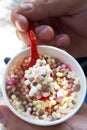 Vertical photo paper cup with multicolored frozen ice cream granules and plastic spoon close-up