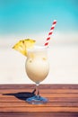 Vertical photo of Pina colada coktail with straw and slice of pineapple on wooden table at the beach