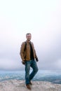 Vertical photo Portrait of a man dressed in a stylish brown leather jacket and jeans. backpack watches and biker gloves. posing on