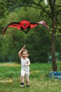 Vertical photo. Positive female child running with red and black colored kite in hands outdoors