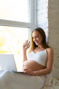 Pregnant woman sits at home in front of a laptop monitor - online consultation with a doctor or online meeting with Royalty Free Stock Photo