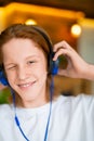 Vertical photo of a red-haired teenager in blue headphones. He listens to music and smiles. Royalty Free Stock Photo