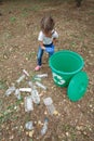Child in blue latex gloves, throwing plastic bag into recycling bin. Land and rubbish on the background. Royalty Free Stock Photo