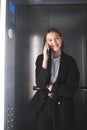 Vertical photo of smiling young businesswoman is talking on her smartphone in the elevator. Positive female office worker is in