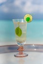 Vertical photo of tasty icy tropical cocktail with lime on the glass table at the beach with ocean Royalty Free Stock Photo