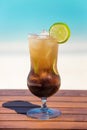 Vertical photo of tropical brown color cocktail with lime on the wooden table at the beach with ocean Royalty Free Stock Photo