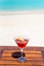 Vertical photo of the tropical red color cocktail with piece of orange on the wooden table at the beach and ocean