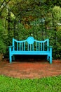 Vertical photo of a vivid blue colored wooden bench on terracotta brick pathway