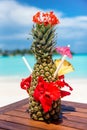 Vertical photo of whole fresh pineapple cocktail with straws, flowers and umbrella on wooden table ocean background at the beach Royalty Free Stock Photo
