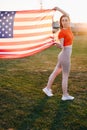 Vertical Photo Woman in Red Sports Top, Tights Holding American Flag Waving in Wind in Full Length Royalty Free Stock Photo