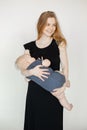 Vertical photo of young blond smiling woman in black dress, holding hungry baby in arms. Using breastfeeding formula. Royalty Free Stock Photo