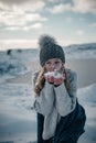 Young woman is blowing a handful of snow in a sweater and hat.