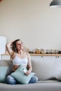 Vertical photo of a young woman sitting on sofa in home clothes and satisfactorily fixing her hair with her hand with her eyes Royalty Free Stock Photo