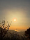 Moody Sunset View of the Sun Glowing Through Hazy Mountain Mists and Bare Trees Royalty Free Stock Photo
