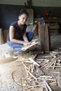 Vertical photograph of a smiling woman crouching on the ground gathering freshly cut firewood to make a fire. equality at work.