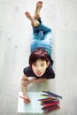 Vertical picture of drawing short haired mocking girl with pencils lying on floor. Idea how to spend time during quarantine in Royalty Free Stock Photo