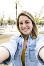 Vertical picture of a gorgeous cheerful blond hair female carefree and satisfied taking a selfie outside. Handsome happy