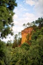 Vertical picture of hiking path Ochre Trail in a natural colorful area of orange cliffs surrounded by green forest in Roussillon, Royalty Free Stock Photo