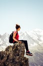 Vertical picture of young female traveller sitting on the edge of rocks. High mountains in background. Woman backpacking. Hiking