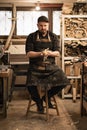 Vertical playful male carpenter pressing in hands wood shaving chips, sitting on chair after hardworking day in workshop