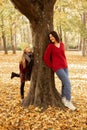 Vertical playful, merry, mischief, happy mother and daughter play and have fun together near tree trunk, hide and seek