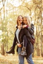 Vertical playful positive, loving, merry family young mother holding daughter on back, promenade in golden autumn forest