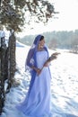 Vertical portrait against the winter landscape of a slender brunette in a long white dress and a beautiful openwork lilac shawl Royalty Free Stock Photo