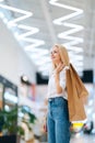 Vertical portrait of attractive blonde young woman holding shopping paper bags with purchases standing in hall of mall Royalty Free Stock Photo