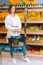 Vertical portrait of attractive young woman customer holding basket of fruits standing at fruit and vegetables section Royalty Free Stock Photo