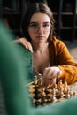 Vertical portrait of attractive young woman in elegant glasses making chess move with knight piece sitting in floor Royalty Free Stock Photo