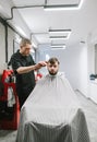 Vertical portrait of a barber and his client in a bright modern barbershop. Hairdresser cuts a bearded man`s scissors. Creating Royalty Free Stock Photo