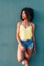 vertical portrait of a beautiful african woman leaning on green wall with summer clothes Royalty Free Stock Photo