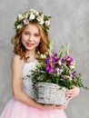 Vertical portrait of a beautiful cute little girl in a wreath of fresh flowers on her head and a basket of beautiful spring Royalty Free Stock Photo