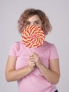 Vertical portrait of beautiful playful woman covers her face with huge colorful round shaped lollipop